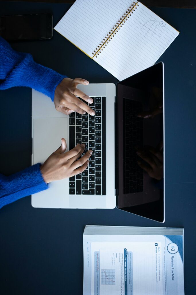 Top view of anonymous female typing on keyboard of netbook with empty black screen on table with notebook